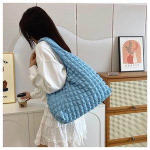 Blue pleated cloud bag with soft puff texture worn by a model in a cozy home setting