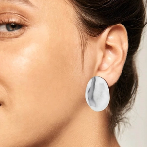 Detailed view of a silver-colored large oval stud earring worn by a female model