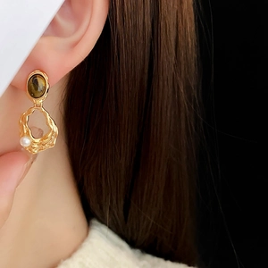Detail view of gold-plated tiger eye earrings with white pearls on female model