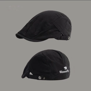 Detail of a black cotton beret featuring embroidered white Womenfly text and bear logo