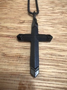 Gros plan du collier croix en acier inoxydable noir texturé sur fond de bois