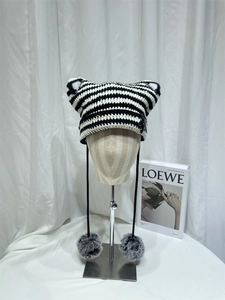 Close-up of black and white striped knitted cat ear beanie with fluffy pompom tassels