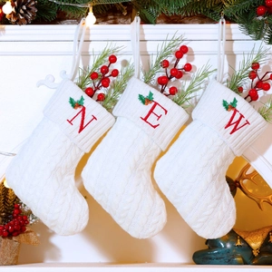 Macro detail of white cable knit Christmas stocking with red embroidered letter and pine decor