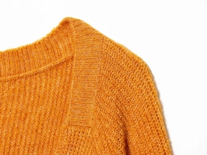 Detailed close-up of orange knit sweater ribbed neckline showing soft wool texture