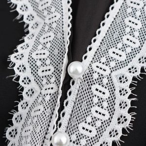 Elegant V-neck dress with black fabric featuring delicate white lace and pearl buttons