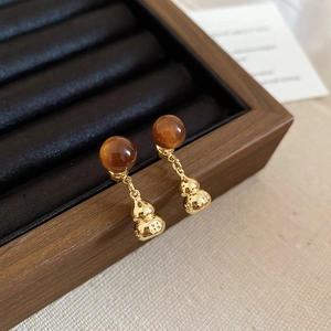 Macro detail of retro gourd drop earrings with amber beads on a wooden display tray