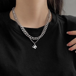 Dettaglio di una collana multistrato argento con catena a maglia e ciondolo con lettera W