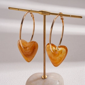 Close-up of heart-shaped amber acrylic earrings on a golden display stand with marble base