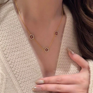 Gold plated zircon flower necklace with red centers worn by a model on a beige sweater
