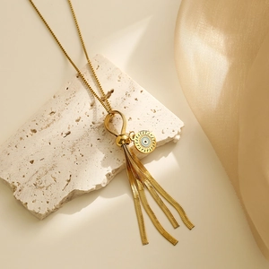 Gold tassel drop necklace with evil eye charm on stone and silk background