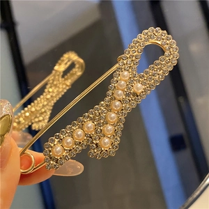 Macro shot of R-shaped gold safety pin brooch with white pearls and sparkling crystals