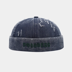Dettaglio del berretto docker in denim blu con ricamo PROGRESS verde e bordi usurati