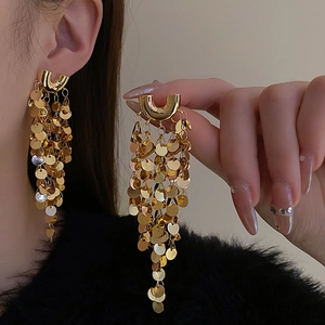 Gros plan sur des boucles d'oreilles dorées en U avec des paillettes et des pompons