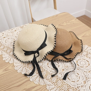 Detail of straw sun hats with black ribbon bows and edge stitching on a wooden table