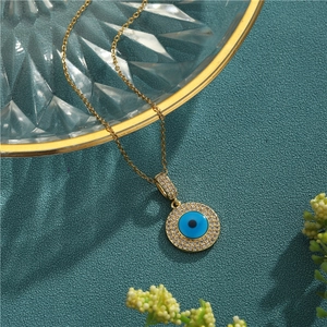 Gold Evil Eye pendant necklace with blue enamel and pavé cubic zirconia on teal background