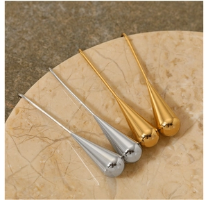 Polished gold and silver teardrop earrings displayed on a beige marble stone base