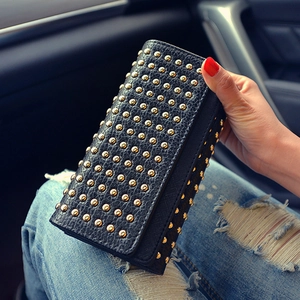 Dettaglio di una pochette lunga in pelle martellata nera con borchie dorate in auto