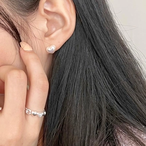 Close-up of heart pearl stud earring and silver heart ring worn by a model