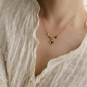 Detailed view of a gold-plated flower pendant with tiger eye stone and pearls on a model