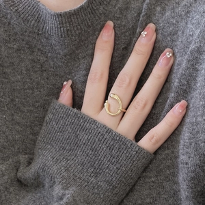 Detailed close-up of a golden fluid-shaped open ring worn on a finger over a dark sweater