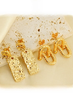Detailed view of hammered titanium steel earrings on a beige stone and silk background