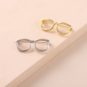Minimalist glasses shaped brooches in gold and silver finish on elegant beige background