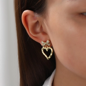 Orecchini a fiocco dorati con pendente a cuore cavo e cristalli sulla modella