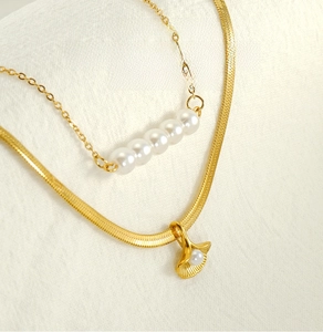 Close-up of dual-layer golden stainless steel necklace with ginkgo leaf and pearls