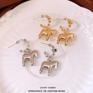 Minimalist metal horse pendant hoop earrings in gold and silver finishes on a ceramic plate