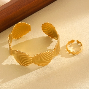 Detailed view of golden seashell bangle and matching ring on sandy textured background