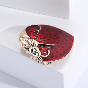 Detail of red enamel cat brooch with black spots, golden edges, and green eyes