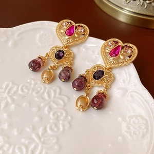 Dettaglio di orecchini barocchi vintage con cristalli rosa e viola su piatto bianco