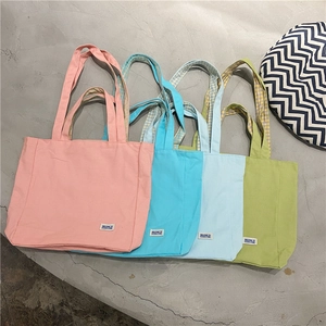 Bolsos de lona en cuatro colores pastel dispuestos sobre una superficie con textura