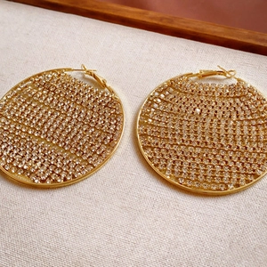 Detailed view of large gold hoop earrings with zircon stones on a beige textured fabric