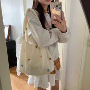 Detail of white canvas tote bag featuring colorful embroidery and delicate lace strap
