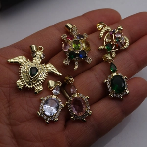 Detailed shot of gold-plated turtle pendants with multi-colored cubic zirconia in palm