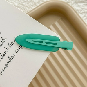 Detail shot of a mint green matte duckbill hair clip on a stylish striped background