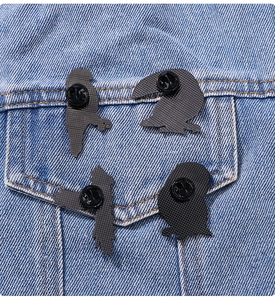 Set of four black bird silhouette enamel pins displayed on a blue denim jacket pocket
