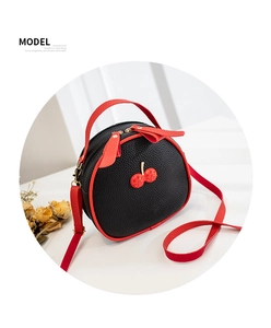Detail of lychee textured leather and sparkling cherry charm on red-black round crossbody bag