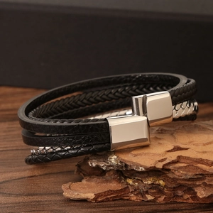 Macro shot of multi-layer black braided leather bracelet with silver magnetic clasp on wood