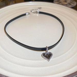 Detail view of a black choker necklace featuring a sparkling heart-shaped crystal pendant