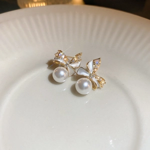 Macro shot of gold bow stud earrings with sparkling crystals and a white faux pearl charm