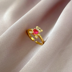 Detail of gold open bear ring holding a red heart crystal on purple silk fabric