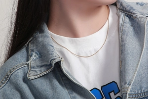 Close-up of minimalist gold snake chain necklace styled with denim jacket