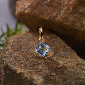 Macro shot of gold S925 silver pendant with square blue gemstone on a brown stone