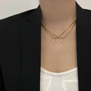 Détail du collier double couche en acier titane doré avec pendentifs lettres L et R scintillants