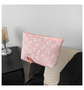 Detail of pink fabric clutch with white floral texture held in a hand featuring gold zipper