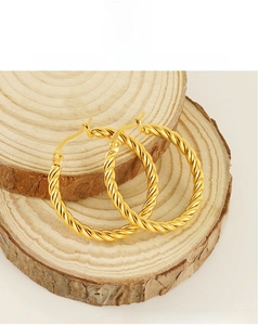 Macro shot of gold twisted rope hoop earrings resting on rustic wooden slices