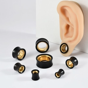 Macro view of black and gold stainless steel ear gauges in various sizes on an ear model