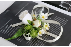 Detail of white artificial rose boutonniere with green leaves and silk ribbon on a book